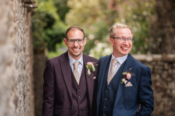 Two grooms beside a barn wall with a lantern, with a garden in the background | Jaye Peg Photography at Holesfoot Cumbria